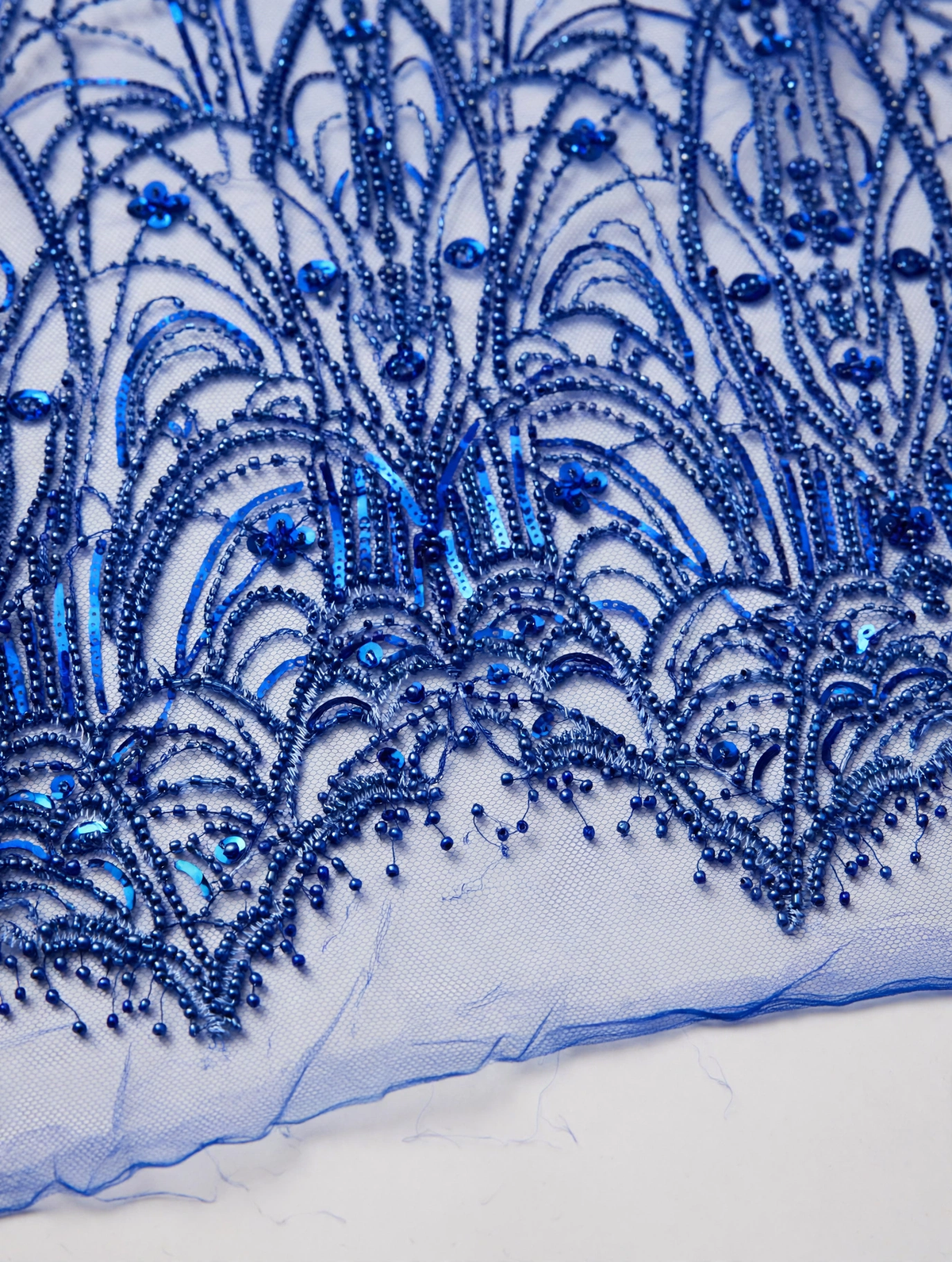 Gros plan des perles et sequins bleu royal formant des éventails et une bordure ondulée sur tulle.