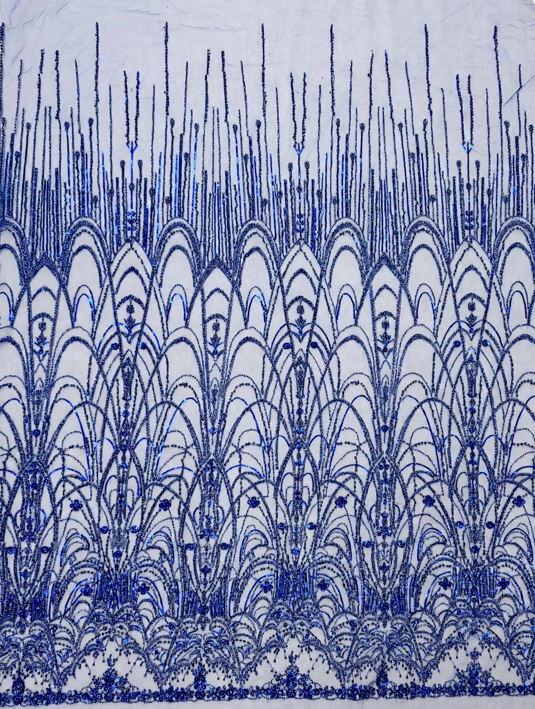 Tulle bleu royal déplié sur fond clair, montrant les éventails perlés, les arches et les lignes verticales.