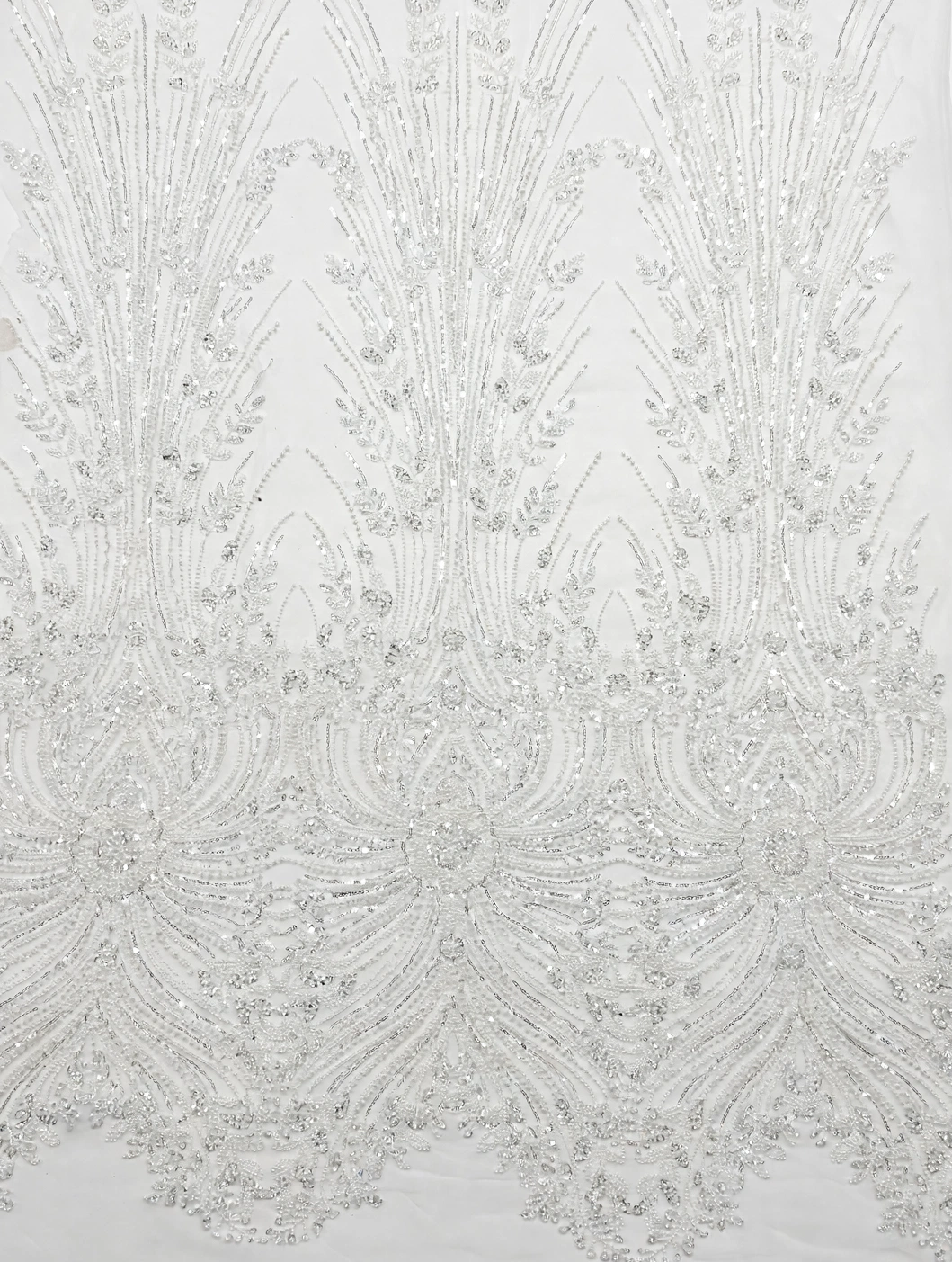 Vue à plat du tulle perlé blanc à longues feuilles et motifs ornementaux brillants.