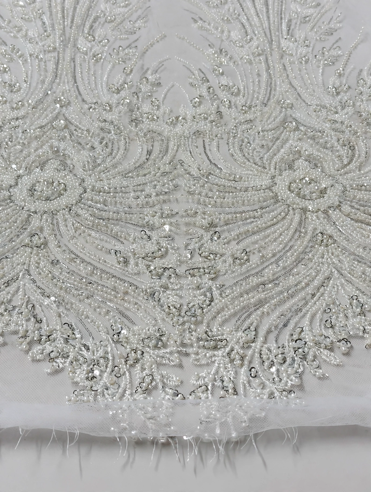 Gros plan du perlage blanc à feuilles et courbes ornées de perles et sequins sur tulle.