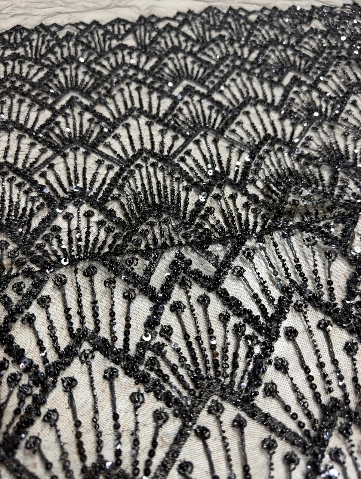Gros plan des perles et sequins noirs dessinant des éventails sur un tulle transparent.